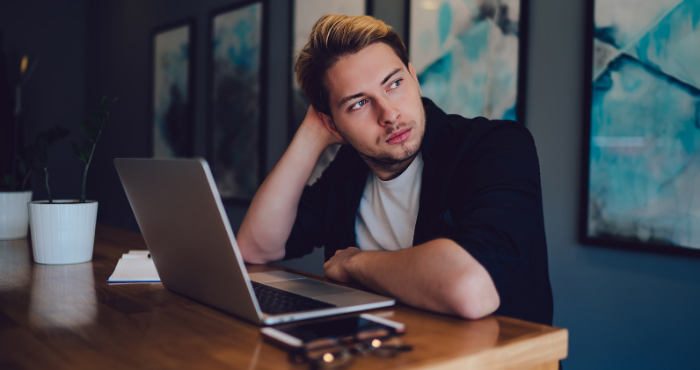 young-man-at-laptop-thinking-looking-outside-window