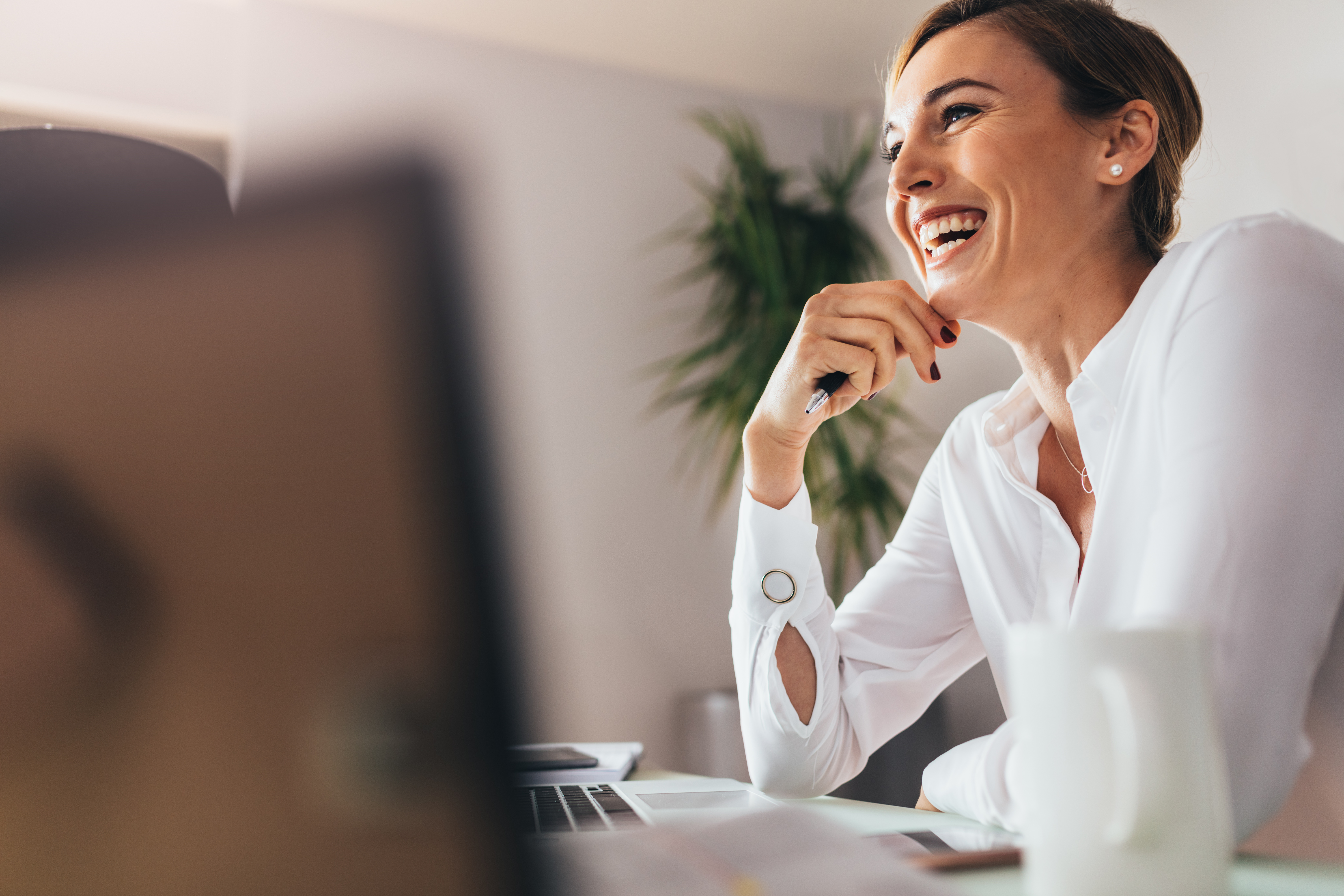 Business woman in office Smiling woman sitting at her desk in office. Happy business woman sitting in office with fingers touching her chin.