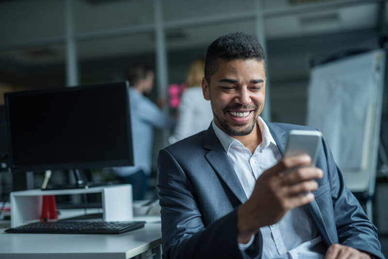Texting with clients Happy african american businessman using a mobile phone in an office.