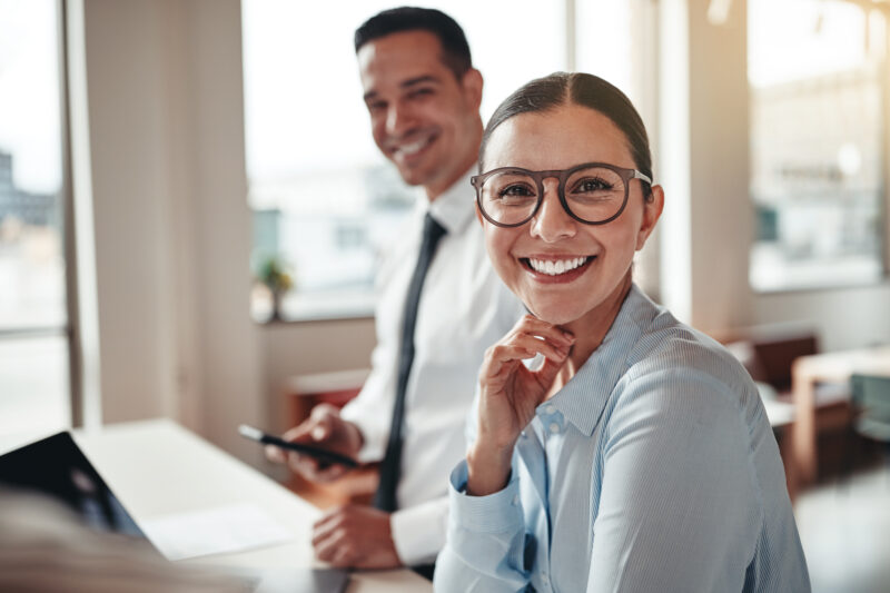 Businesswoman smiling while working with a colleague in an offic Smiling young businesswoman having a meeting with a coworker around a table during a meeting in a modern office