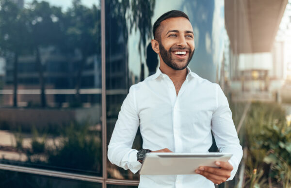 Portrait of a young confident smiling indian man holding a table Portrait of a young confident smiling indian man holding a tablet and looking into the distance