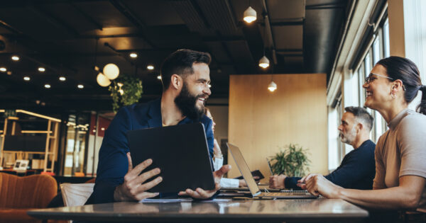 Co-workers smiling at each other in a co-working space Co-workers smiling at each other while sitting at a table in a co-working space. Two happy businesspeople sharing a workspace in an open office. Cheerful young entrepreneurs using wireless technology.
