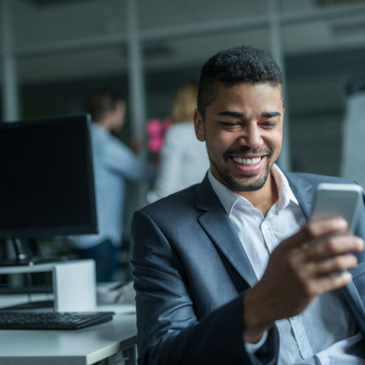 Texting with clients Happy african american businessman using a mobile phone in an office.