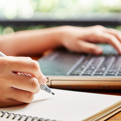 Close up hand of girl writing some data in notebook while studying online course on computer laptop, Learning without school or home education concept