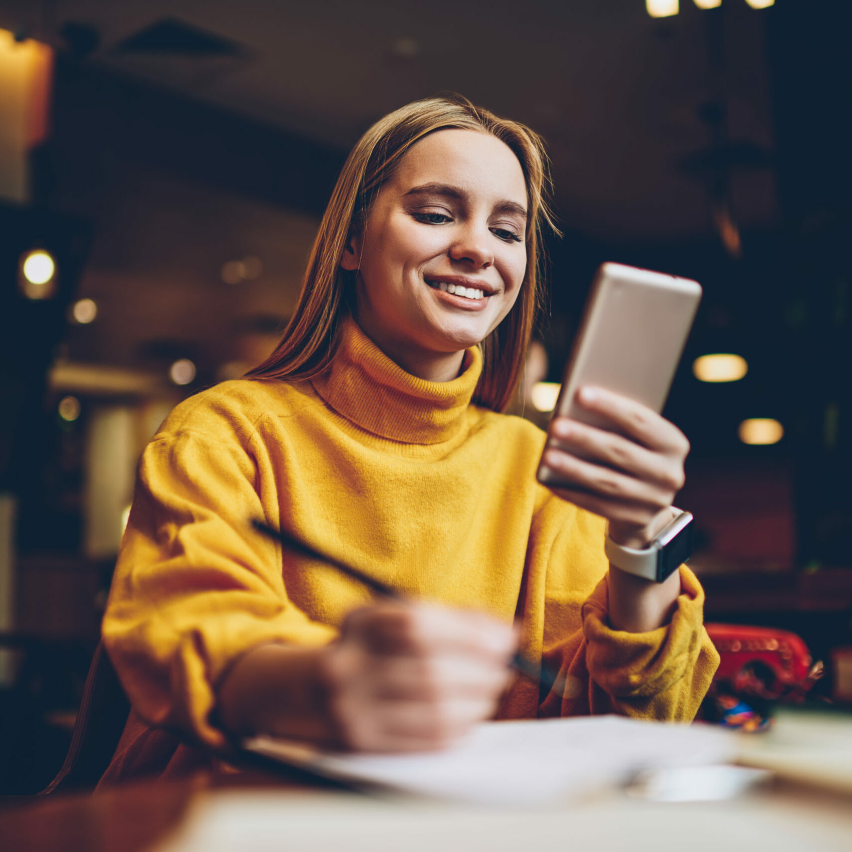 Pretty prosperous blonde woman dressed in cool yellow sweater using smartphone application for planning working schedule.Cute successful female blogger chatting with followers in social network Pretty prosperous blonde woman dressed in cool yellow sweater using smartphone application for planning working schedule.Cute successful female blogger chatting with followers in social network